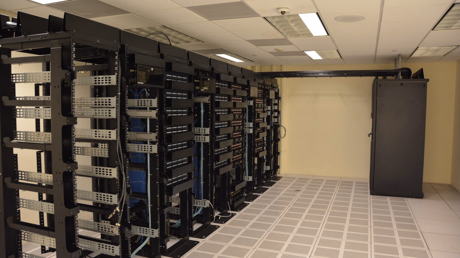 Rows of open network racks on a raised floor of perforated cooling tiles in a data centre room