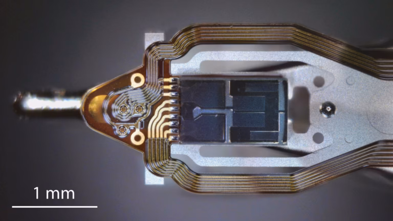 Microscope view of a hard disk drive read-write head slider on its gimbal with gold flex-circuit traces, with a 1 mm scale bar