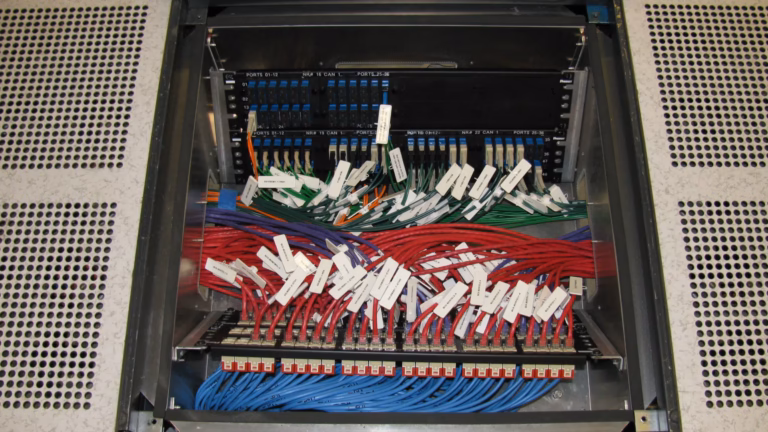 An in-floor patch panel in a computer room, with a fibre connector panel above rows of labelled red, green and blue patch cables