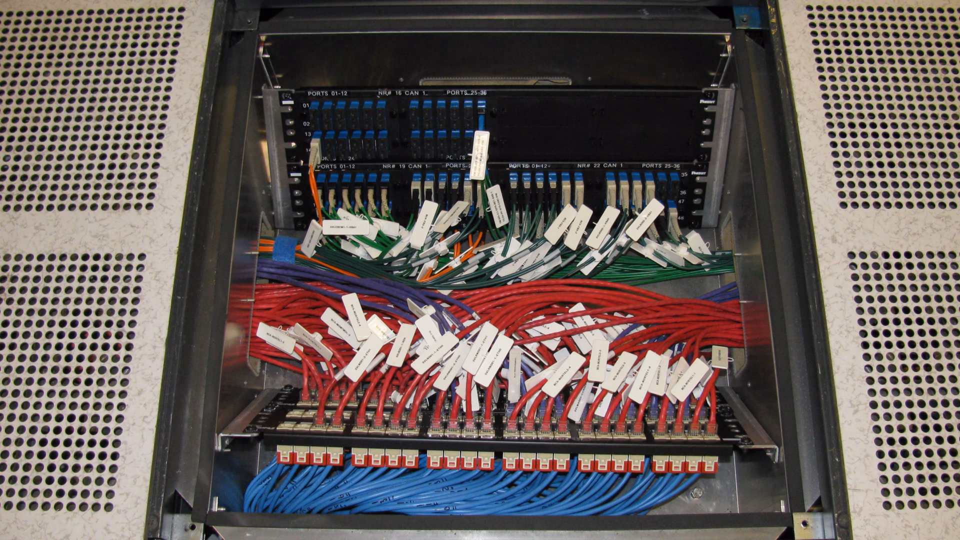 Un pannello di permutazione a pavimento in una sala macchine, con un pannello di connettori in fibra sopra file di cavi di permutazione etichettati rossi, verdi e blu