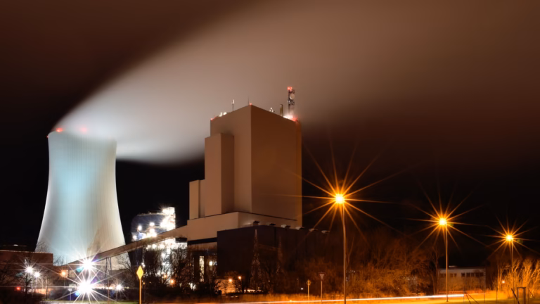 Night view of the Rostock power station in Germany, its cooling tower releasing a long plume of water vapour