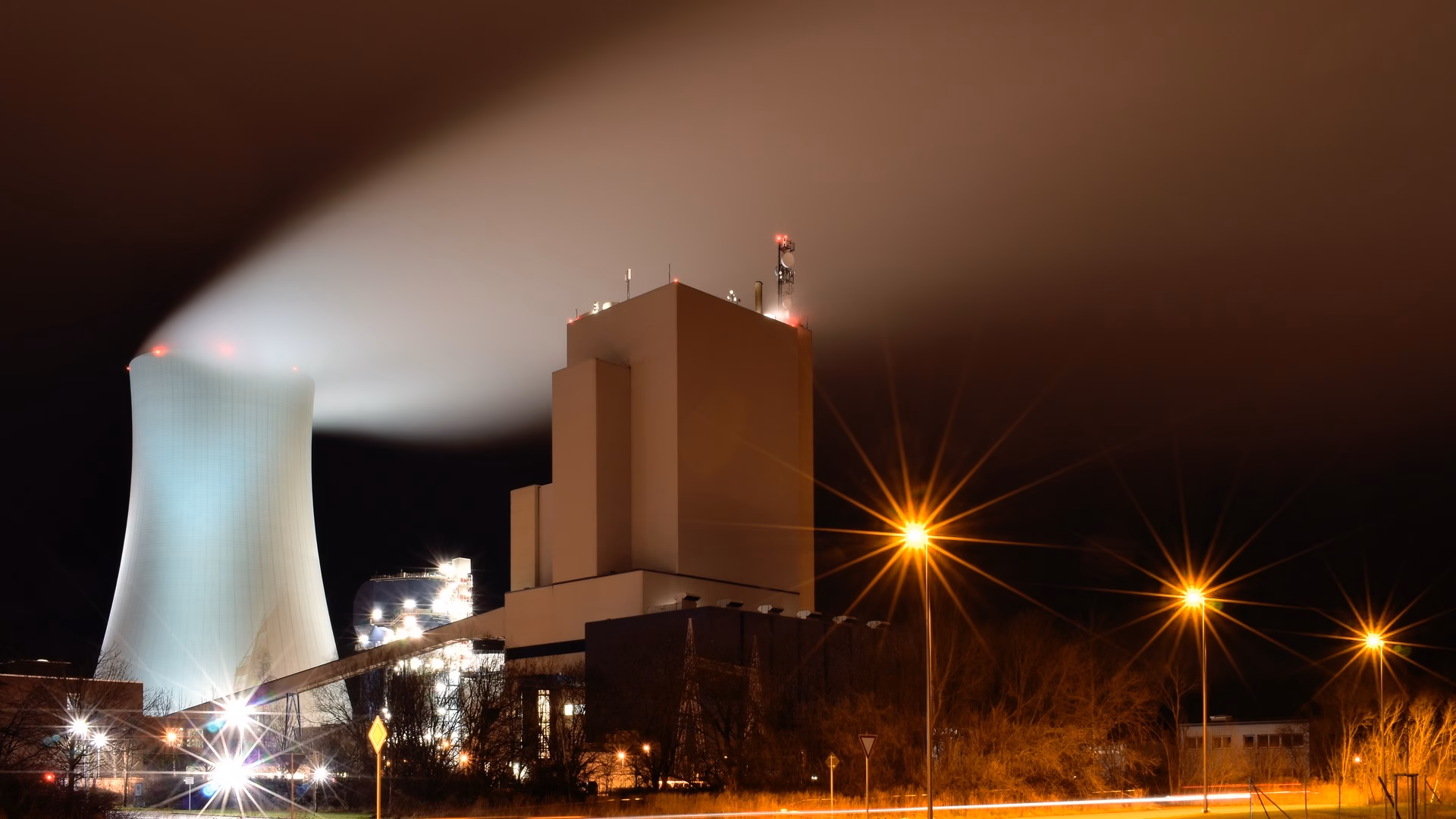 Night view of the Rostock power station in Germany, its cooling tower releasing a long plume of water vapour