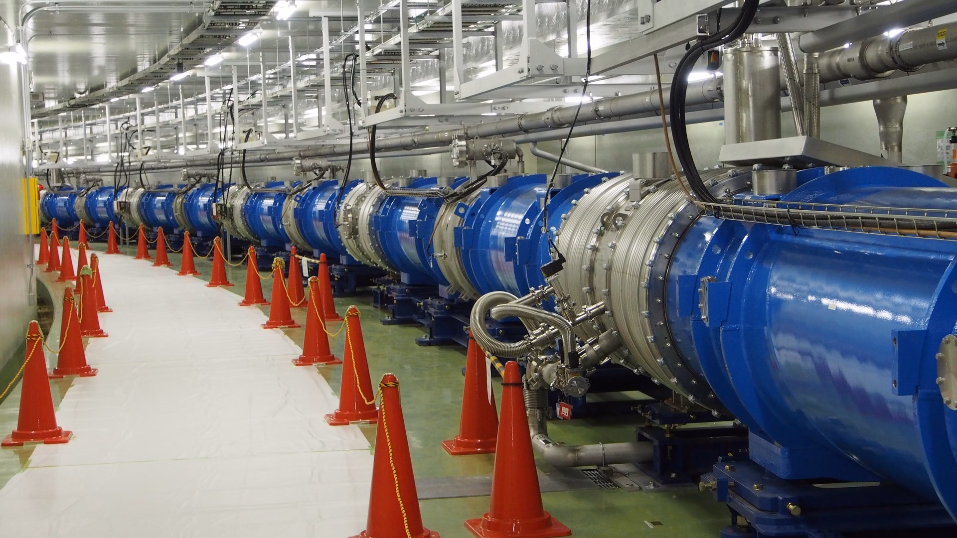Magneti superconduttori lungo la linea di fascio primaria di protoni del complesso di acceleratori J-PARC in Giappone, con coni di sicurezza sulla passerella
