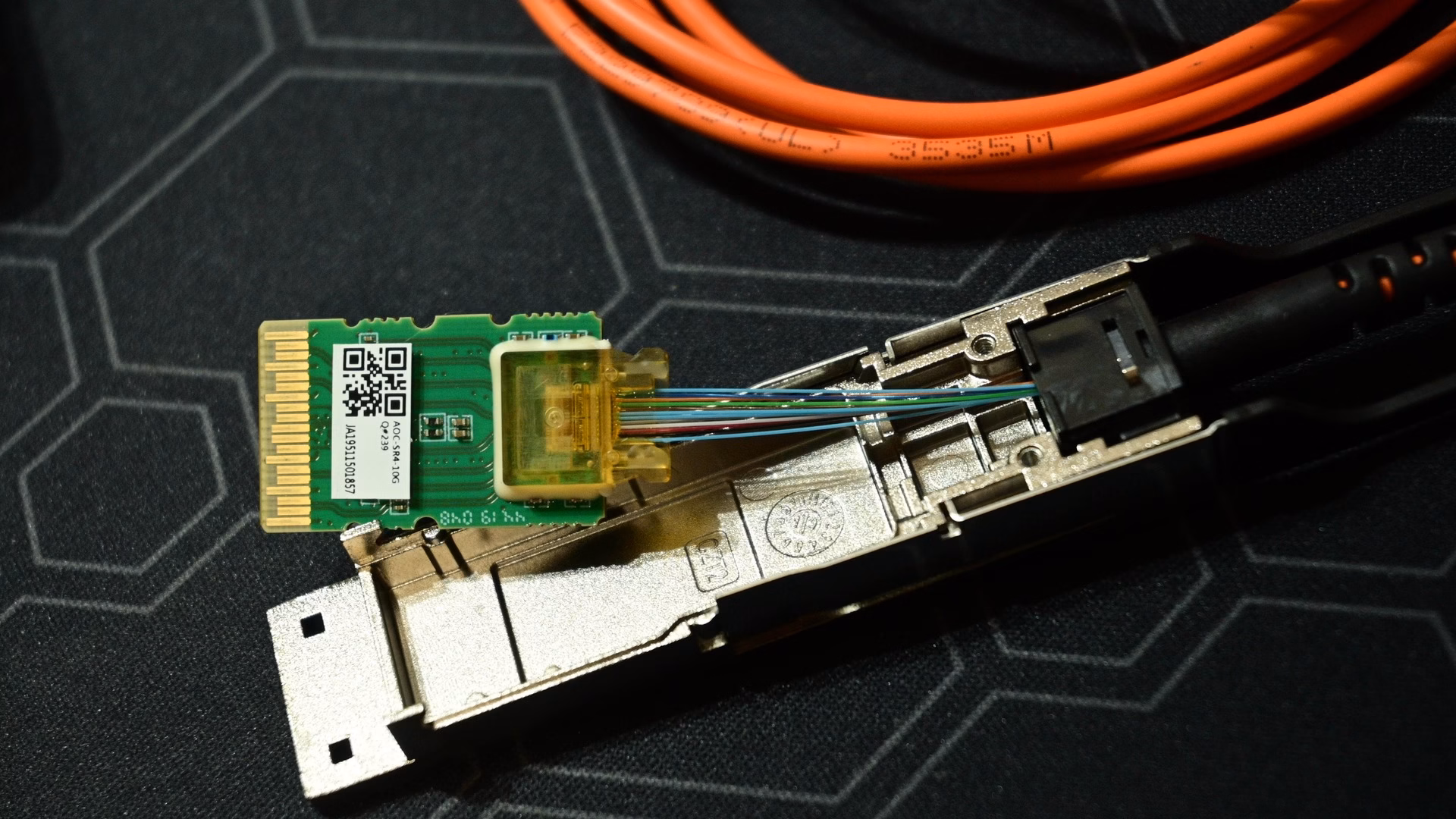 A 40-gigabit QSFP pluggable optical transceiver opened up, showing its small circuit board, optical engine and the colour-coded fibres leading to the cable