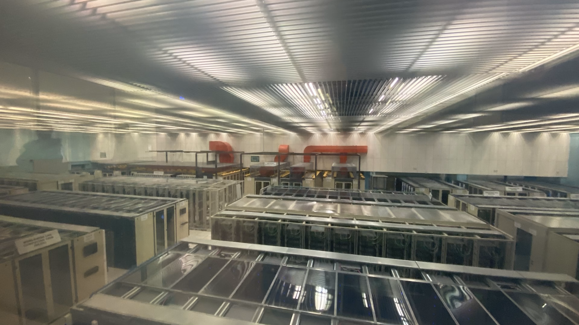 Rows of server and storage racks in the CERN data centre in Geneva, seen through a viewing window.