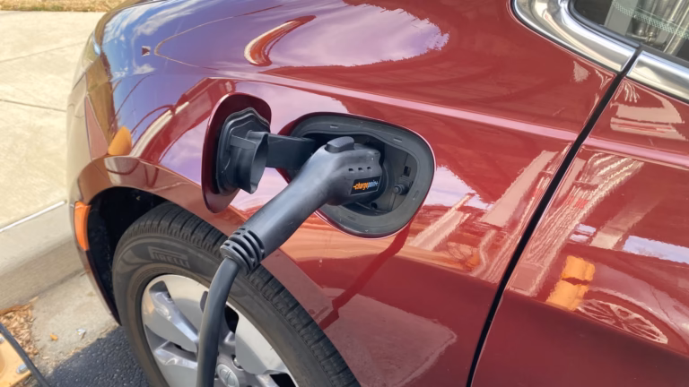A charging connector plugged into the charge port of a red plug-in hybrid car