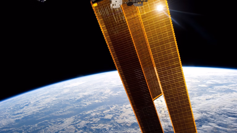 Gold solar array wings of the International Space Station catching direct sunlight above the curve of the Earth