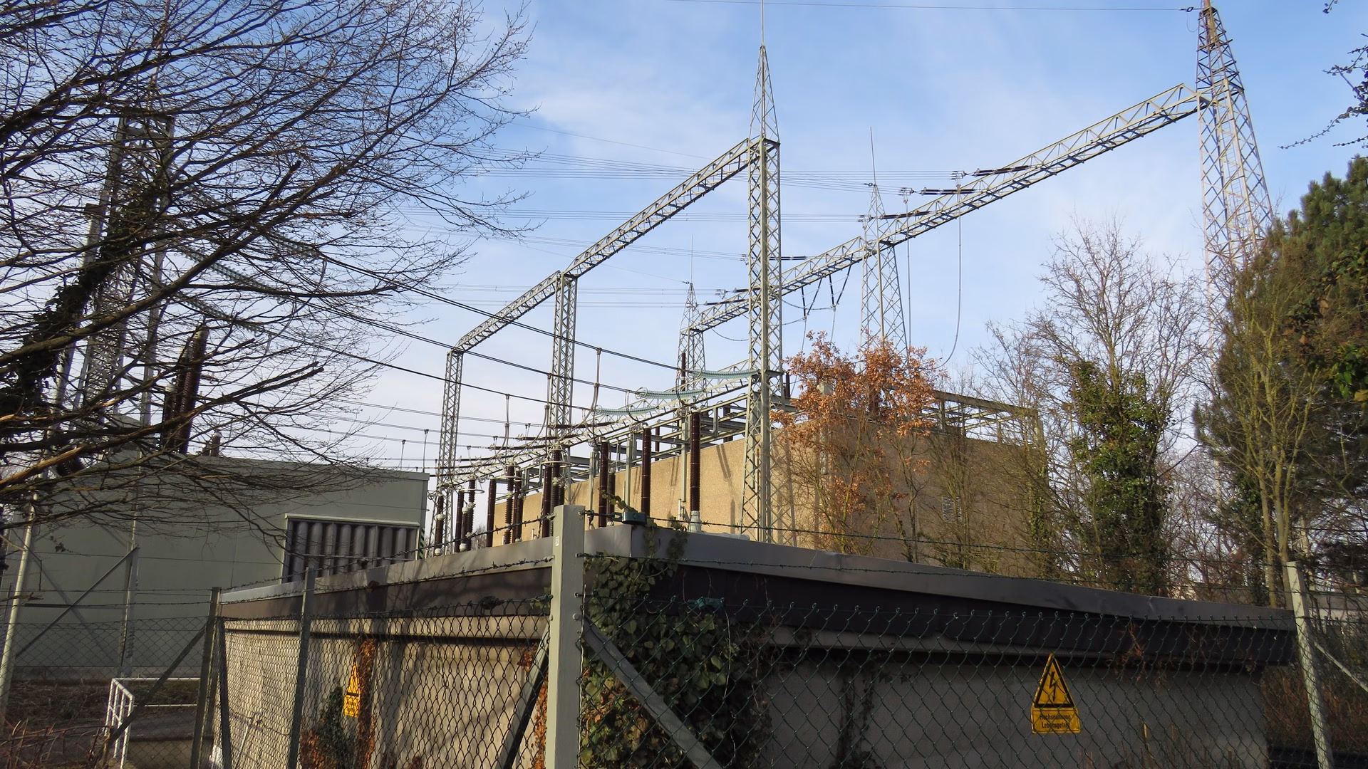 The 380/110 kV Frankfurt-Südwest substation in Frankfurt-Griesheim: lattice gantries and overhead lines above a fenced switchyard under a blue winter sky.