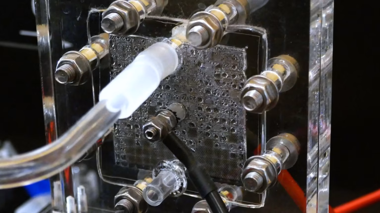 Close-up of a transparent proton exchange membrane fuel cell at the Deutsches Museum, with water droplets on the flow field behind the gas fittings