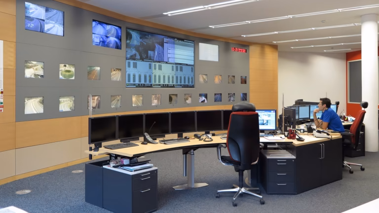 An operator watches a wall of CCTV feeds from a desk in a remote monitoring control room
