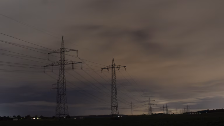 High-voltage transmission towers and lines crossing dark fields at night under a cloudy sky, near Oberjettingen in southern Germany.