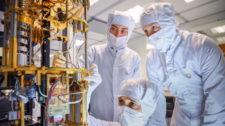 Three researchers in cleanroom suits assembling the gold-plated cryogenic stage of a superconducting quantum computer