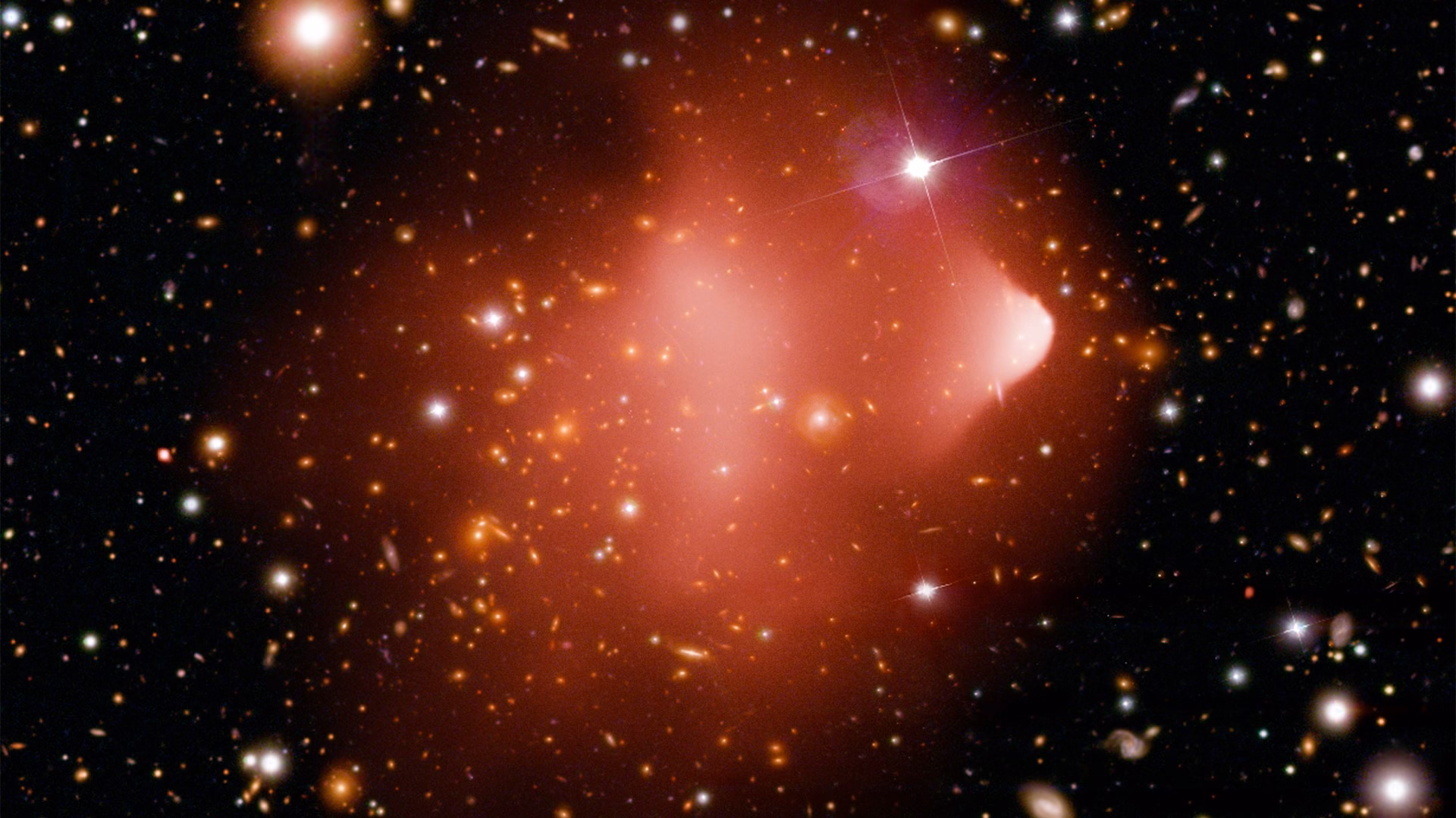 The Bullet Cluster, two colliding galaxy clusters, with hot X-ray gas shown in pink over a field of galaxies, an object used to test ideas about dark matter and antimatter