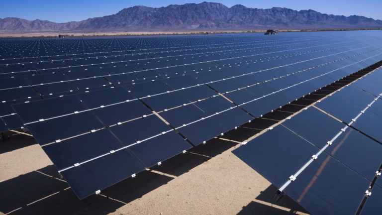 Rows of photovoltaic panels stretching toward the mountains at a utility-scale solar plant in the California desert