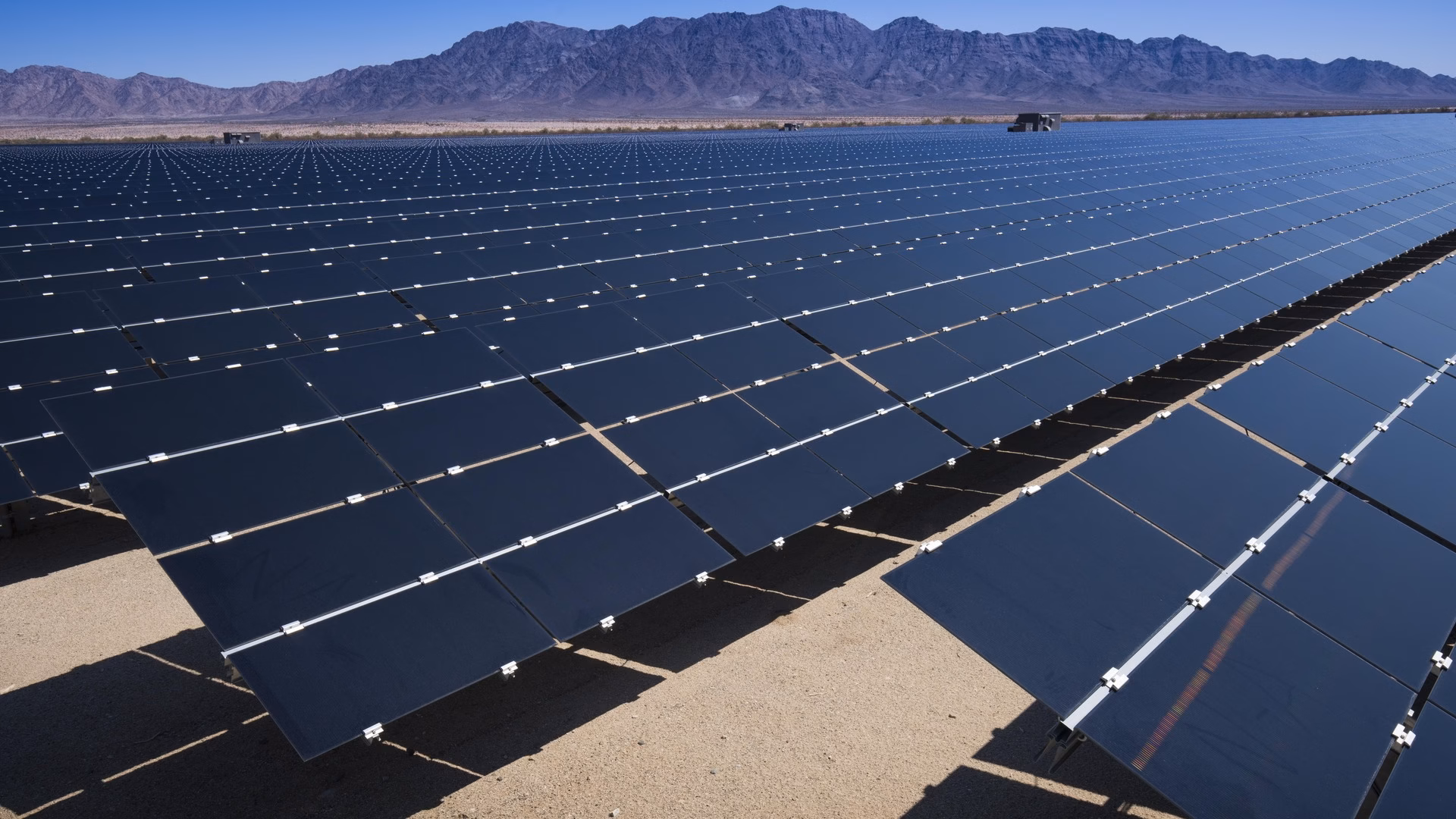 Rows of photovoltaic panels stretching toward the mountains at a utility-scale solar plant in the California desert