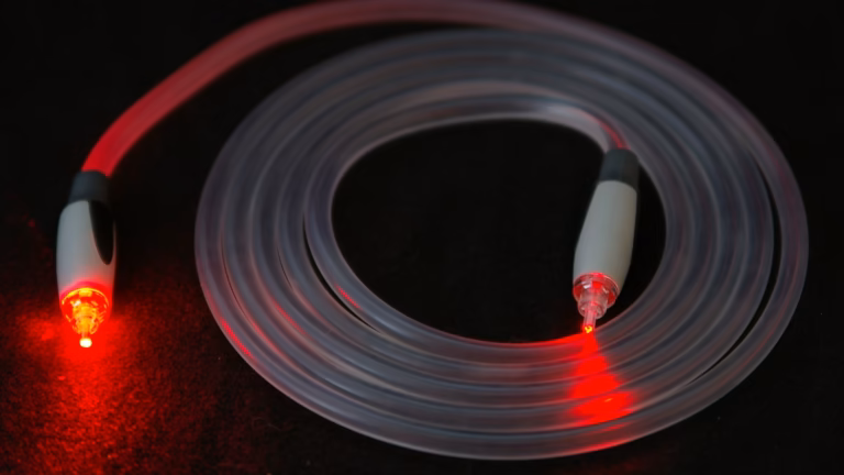 A coiled TOSLINK optical fibre cable on a black surface with red laser light shining out of both connector tips