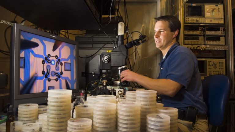 A Sandia National Laboratories researcher at a probe station measures the wavelength of a vertical-cavity surface-emitting laser, whose bright emission spot appears magnified on the monitor