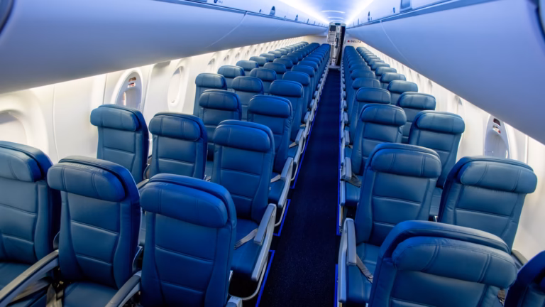Empty rows of blue economy seats receding toward the rear of an Airbus A220 cabin on either side of the aisle