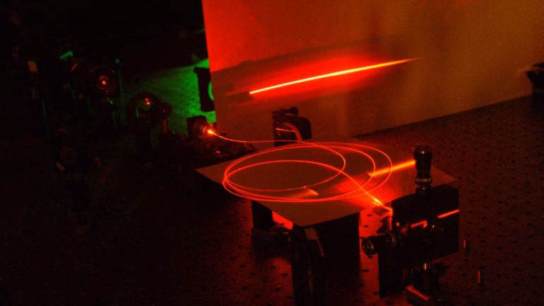 A coiled microstructured optical fibre glows red on the optical table of a NIST paired-photon source built for quantum communication