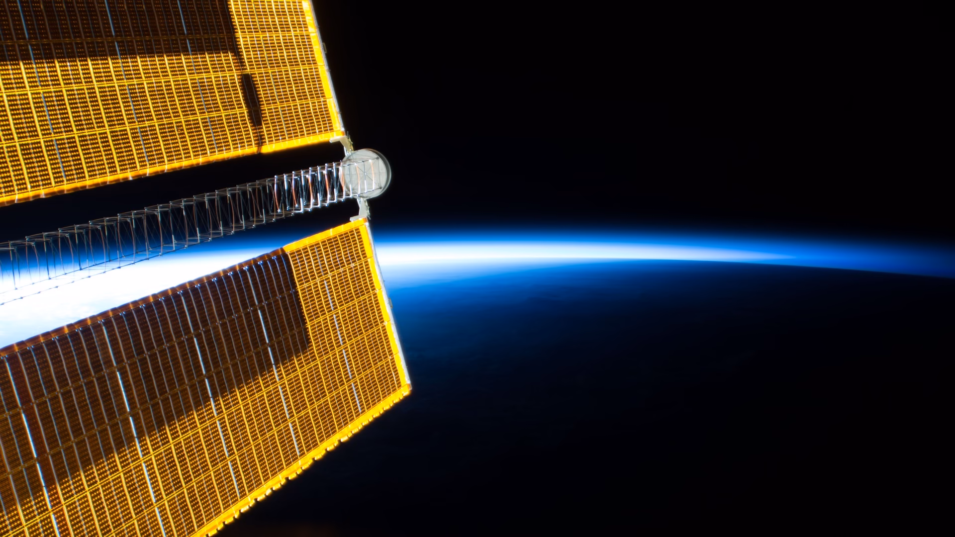 A solar array of the International Space Station against the blue glow of Earth's horizon, photographed in July 2018